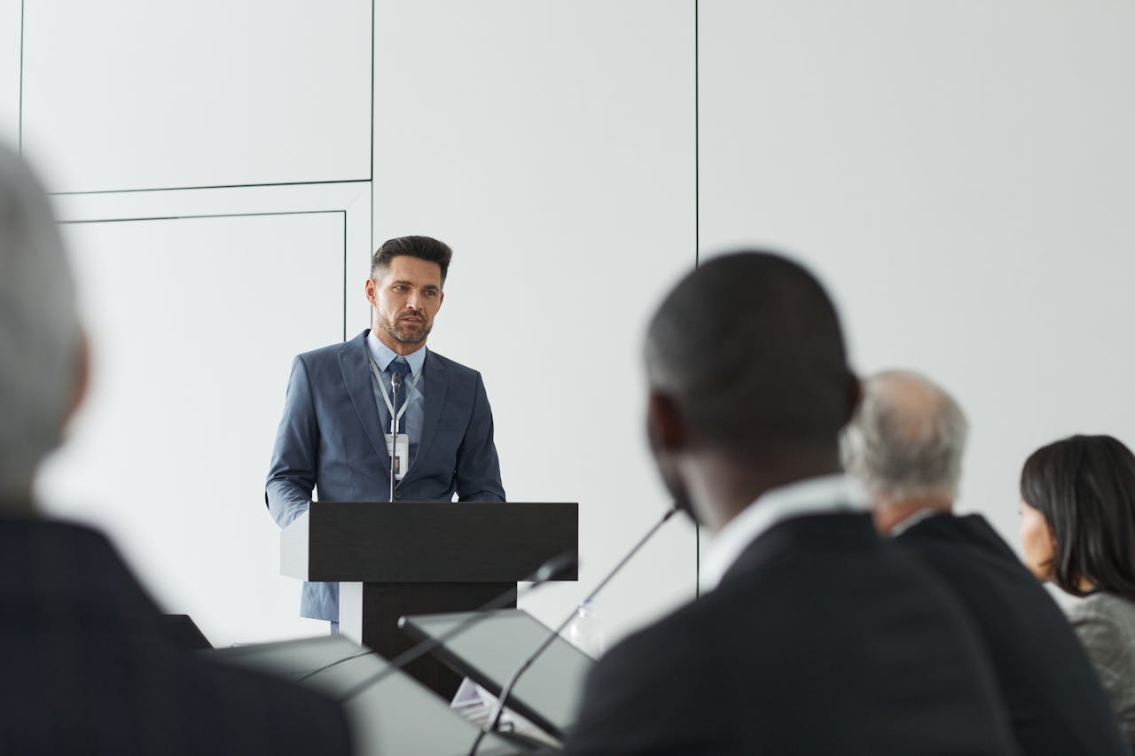 Speaker at a conference delivering a presentation to a diverse audience in a modern setting.