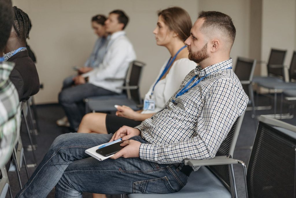 Adults attending a business seminar, attentively listening with notebooks and smartphones.